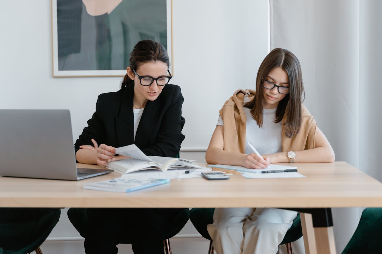 About Two women working together with books and a laptop, focused on learning.